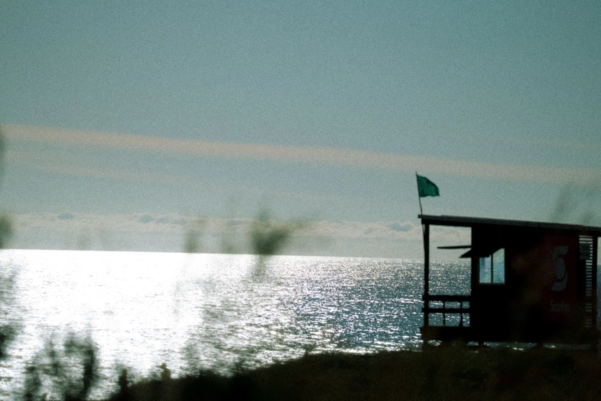 Posto salva-vidas e bandeira verde sobre o mar prateado