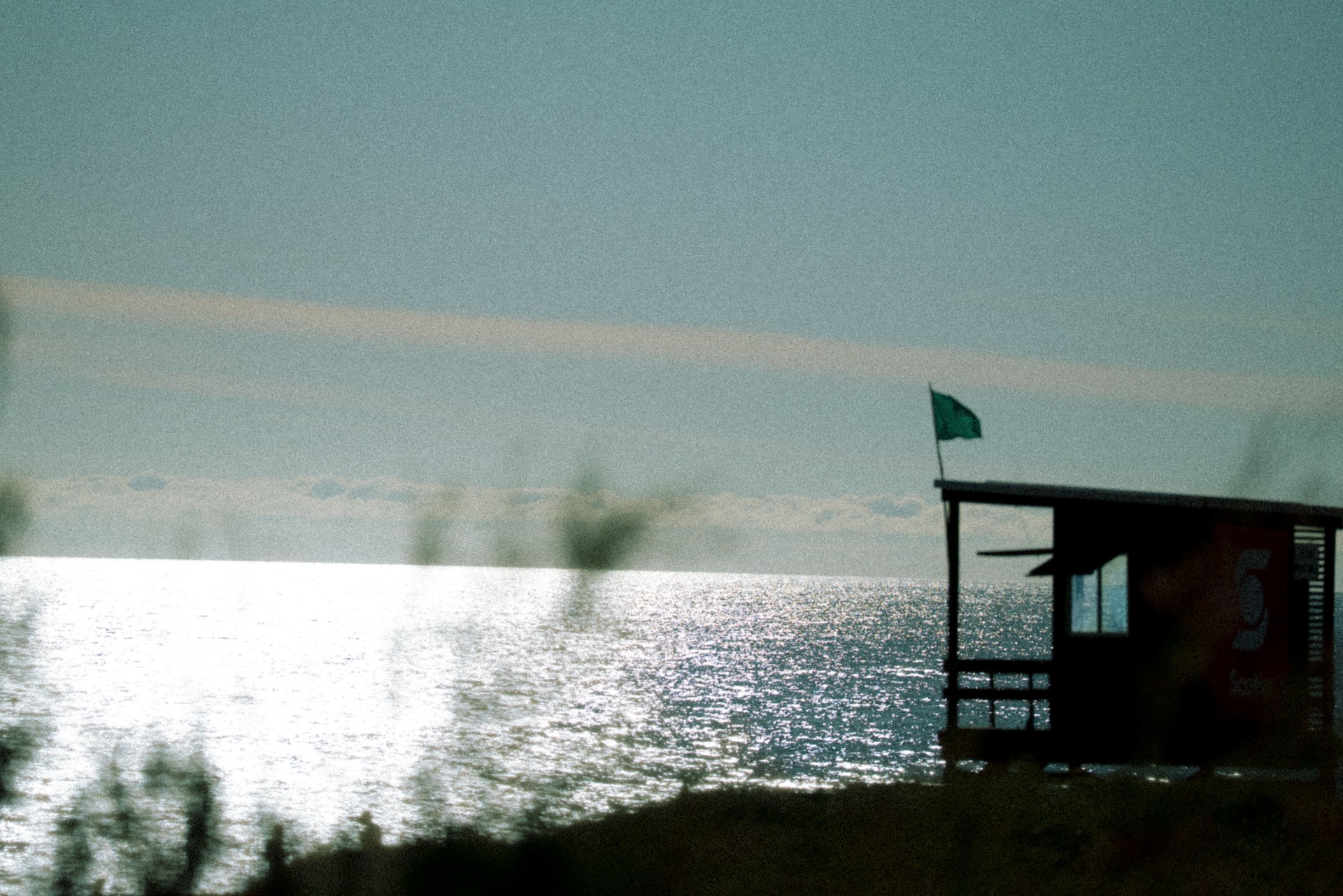 Posto salva-vidas e bandeira verde sobre o mar prateado